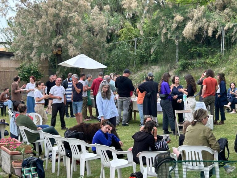 Una festa in campo: persone sedute e in piedi sul prato, all'ombra di un ombrellone