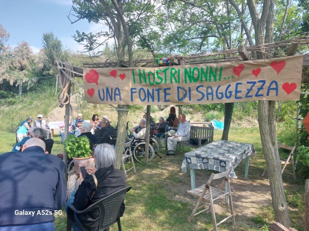 I nonni seduti all'ombra in campo, sotto lo striscione «I nostri nonni, una fonte di saggezza»
